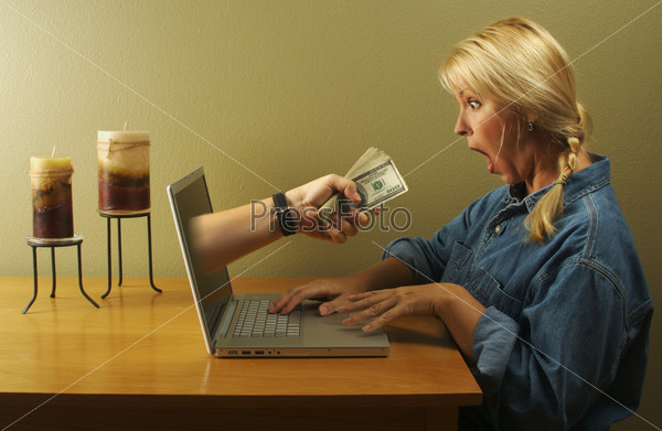 Attractive business woman shocked to see a hand coming through her laptop screen handing her lots of money. Can it be that simple?