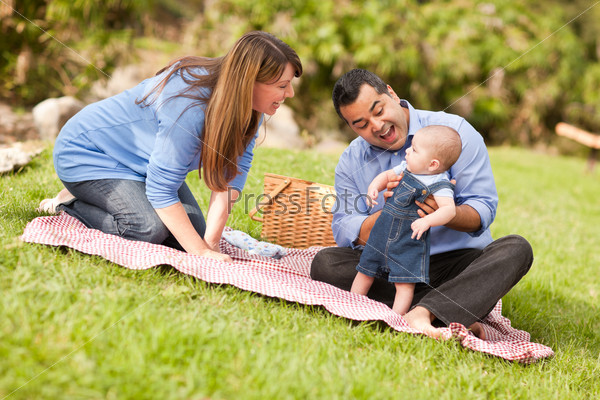 Happy Mixed Race Family Having a Picnic and Playing In The Park.