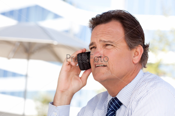 Confident, Handsome Businessman Smiles as He Talks on His Cell Phone Outdoors.