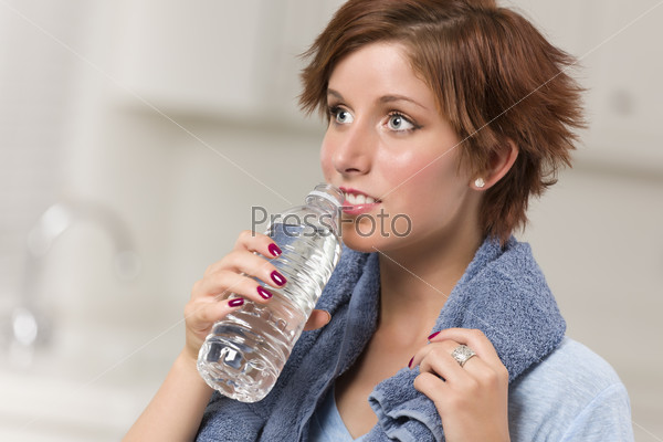 Pretty Red Haired Woman with Towel Drinking From Water Bottle in Her Kitchen.