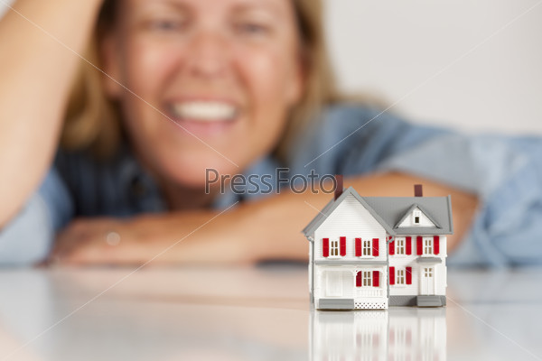 Улыбающаяся женщина позади модели дома на белой поверхности