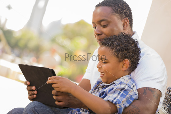 Happy African American Father and Mixed Race Son Having Fun Using Touch Pad Computer Tablet Outside.
