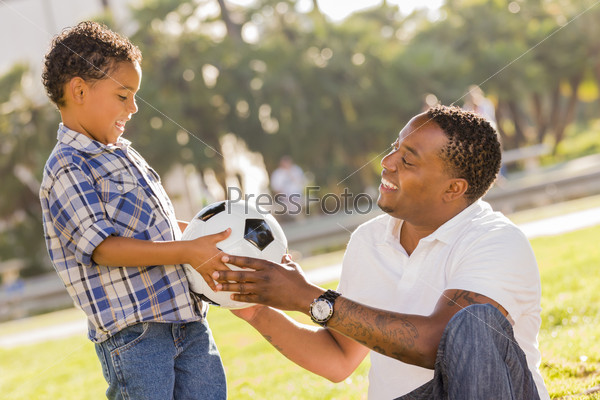 African American Father Hands New Soccer Ball to Mixed Race Son at the Park.