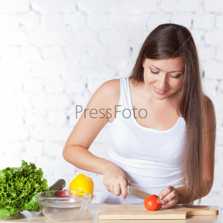 happy brunette woman cutting  fresh tomato over white brick wall