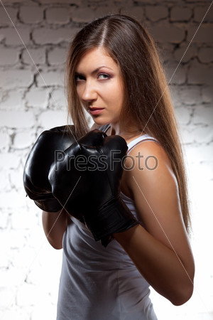 brunette woman wearing boxer gloves over brick wall with flying hair
