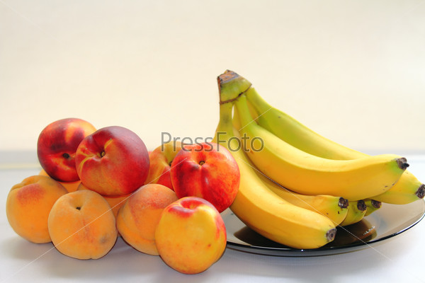 Красивые вкусные персики и бананы на светлом фоне