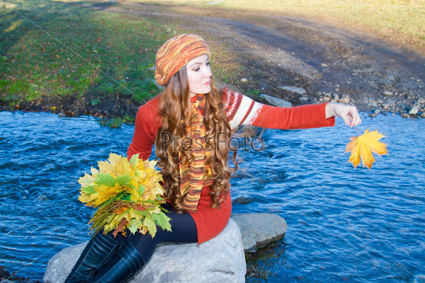 beautiful girl with long curly hair into knitted garments cast a maple leaf in the river fall
