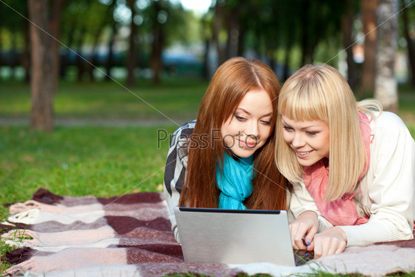 Two sisters with laptop laying in the summer park, stock photo