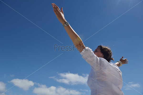Happy young woman with spreading arms, blue sky with clouds in background - copyspace, stock photo