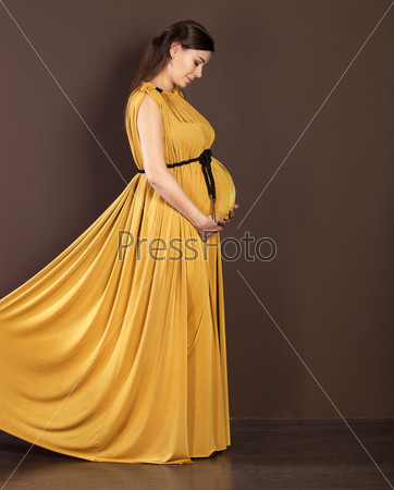 Happy pregnant woman in beautiful long dress touching her belly