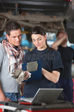 Female mechanic explaining cost to the client standing next to her with person in background