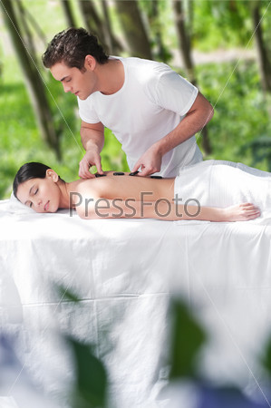 Man giving a hot mineral sacred stone treatment to a woman