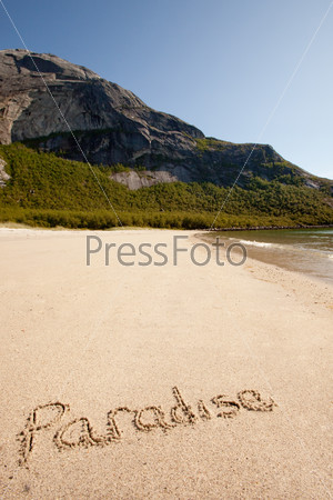 The word paradise written in the sand on a beautiful island