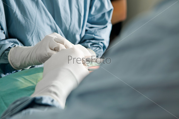 Two people in scrubs with a detail shot of their hands working in a surgery