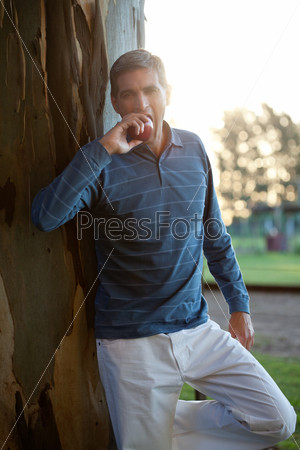 Portrait of casual middle aged man eating apple while standing near tree trunk