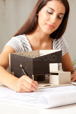 A young female architect working on blueprints with a model house