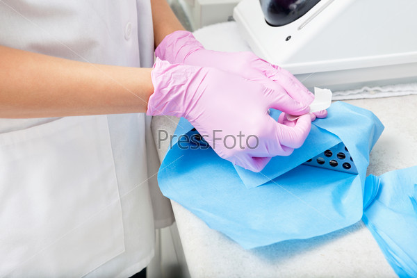 Closeup of a gloved female doctor`s hands wrapping a sterile box of medical instruments