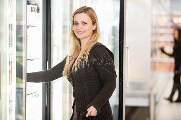 Smiling woman in front of refrigerator looking at camera with person in the background