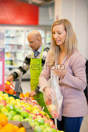Young woman buying fruits with shop assistant in the background