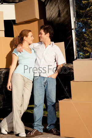 A happy couple in front of a moving van filled with cardboard boxes