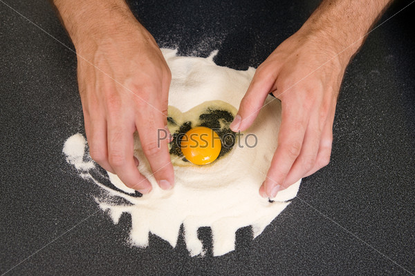 A young man making pasta at home in an apartment kitchen.  An above view of an egg in flour ready to be mixed by hand.