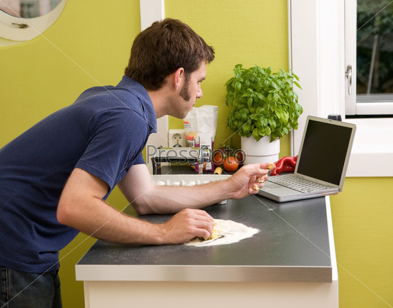 A young cook at home in an apartment kitche, looking on the computer at a recipe while making fresh pasta.