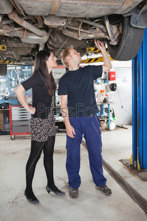 Young male mechanic and woman looking at underboy of car in auto repair shop