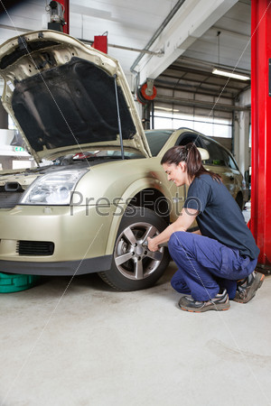 Female mechanic changing wheel of car with pneumatic torque wrench