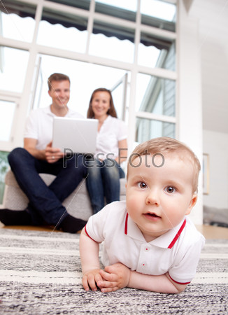 A happy curious young baby boy with parents in the background using computer