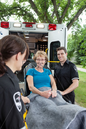 Two ambulance workers pushing a happy senior woman on a stretcher