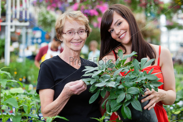 Young woman with her grandmother holding potted plant with people in background