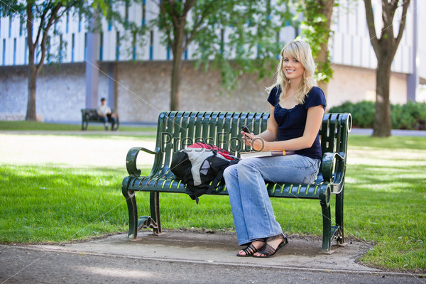 Young female student holding cell phone while sitting in college campus