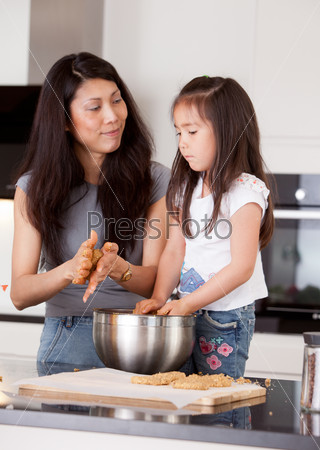 Mother and daughter rolling cookie dough together in kitchen
