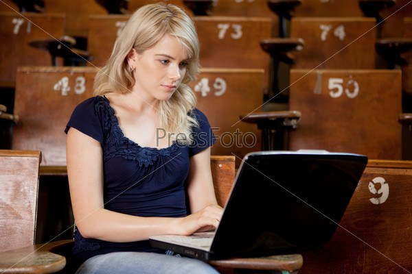Pretty young university girl taking notes on a laptop computer