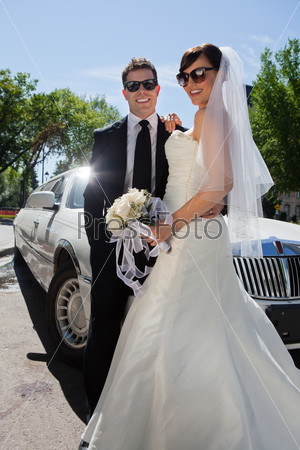 Newly wed couple in sunglasses standing near limousine