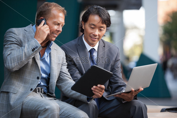 Businessmen using laptop and tablet pc while communication on cell phone
