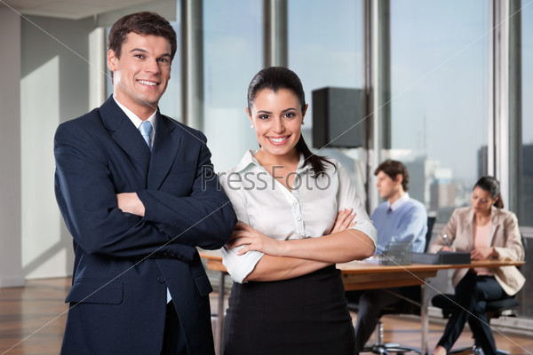 Portrait of business executives with arms crossed with colleagues working in background