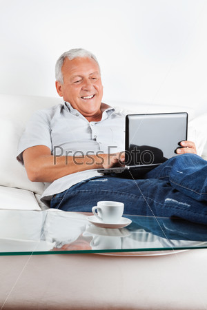 Relaxed senior man sitting on sofa working on laptop at home