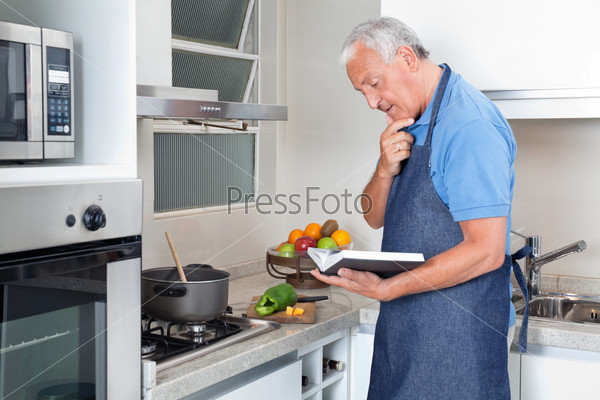 Senior man preparing food with the help of recipe book