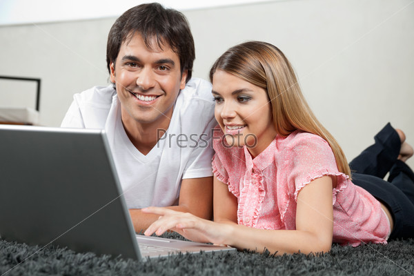 Portrait of young couple lying on rug comfortably with laptop