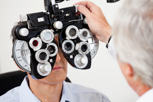 Optometrist performing eye test with phoropter on a male patient