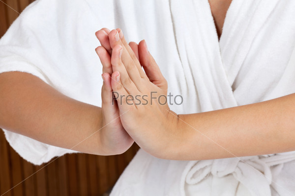 Midsection of a woman in white bathrobe meditating with hands clasped