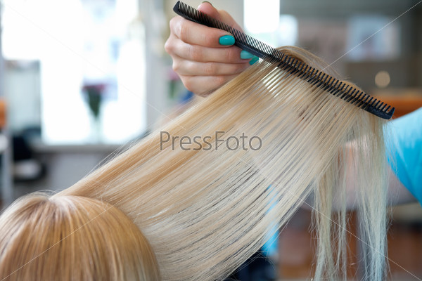 Cropped image of hairdresser\'s hand combing hair of female customer at salon