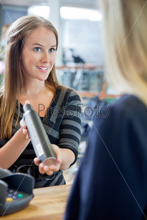 Young female hairstylist showing hair product to customer at counter