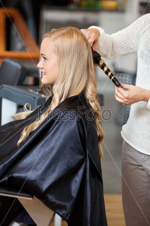 Side view of a young woman getting her hair curled by beautician at parlor