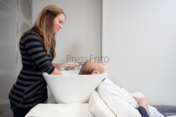Relaxed young woman wrapped in towel getting a hair wash in salon by hairdresser