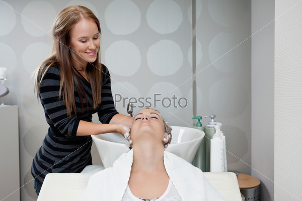 Pretty female beautician washing customer s hair before a haircut at beauty salon