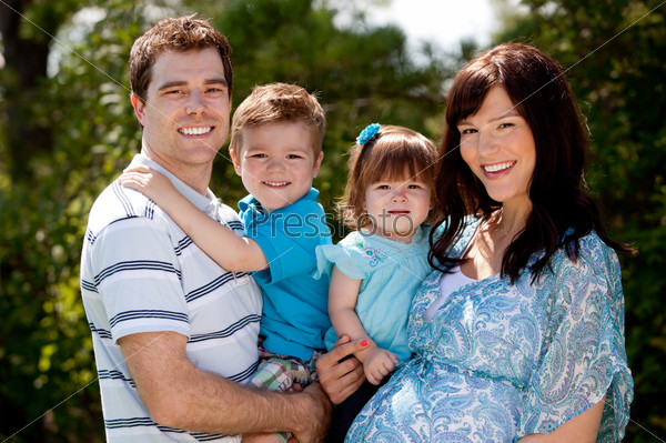 Outdoor portrait of a happy young family with pregnant mother