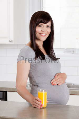Pregnant woman in third trimester at home in kitchen with orange juice