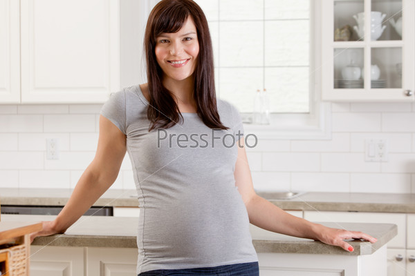 Happy smiling woman in her third trimester at home in kitchen